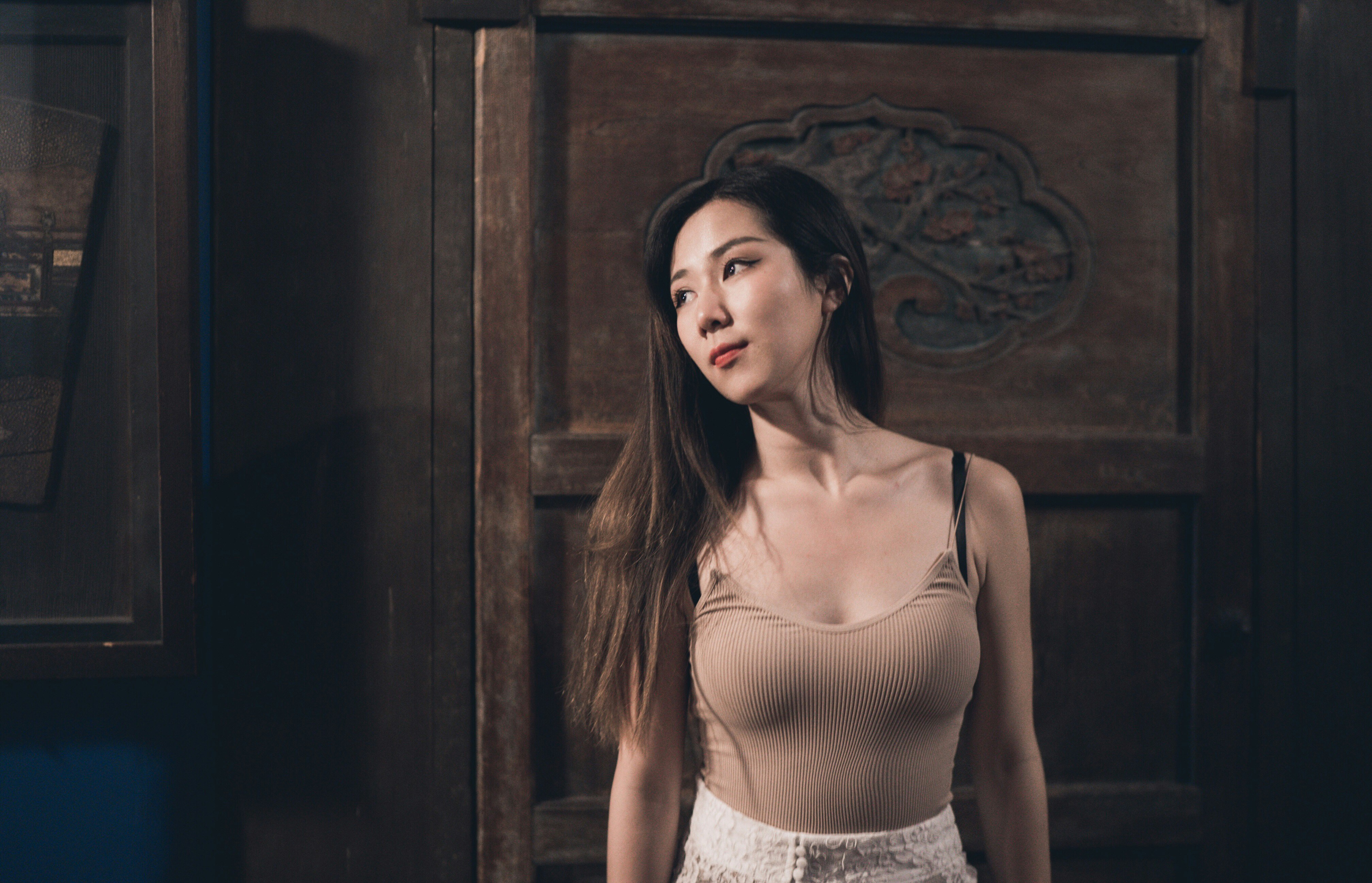 woman in white spaghetti strap top standing near brown wooden door